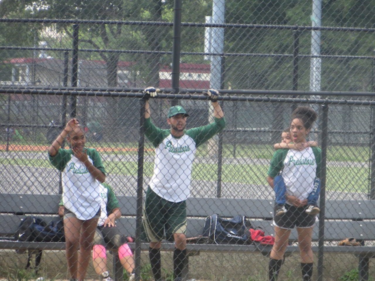 Players in green jerseys by chain-link fence
